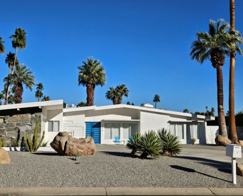 A white mid-century modern home in Palm Springs with a blue door