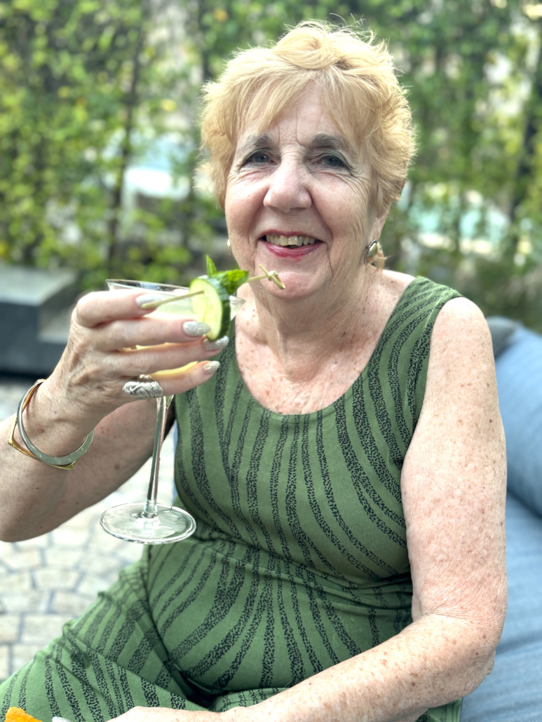A woman wearing a green dress holds up a glass outside at Seymour's