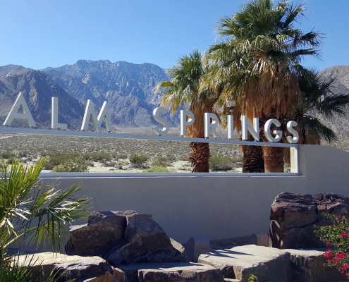 The Palm Springs sign on a windy day with palm fronds blowing in the background