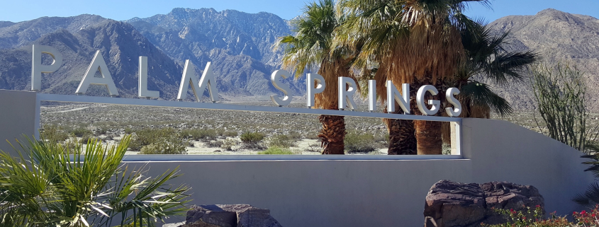 The Palm Springs sign on a windy day with palm fronds blowing in the background