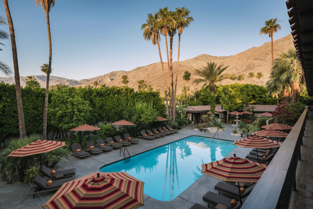 The pool surrounded by striped umbrellas and palm trees at Santiago Resort in Palm Springs, California