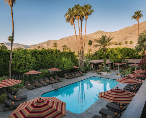 The pool surrounded by striped umbrellas and palm trees at Santiago Resort in Palm Springs, California