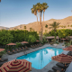 The pool surrounded by striped umbrellas and palm trees at Santiago Resort in Palm Springs, California