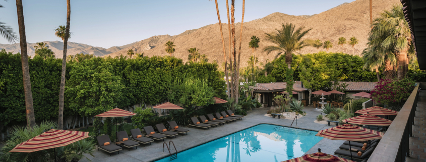 The pool surrounded by striped umbrellas and palm trees at Santiago Resort in Palm Springs, California